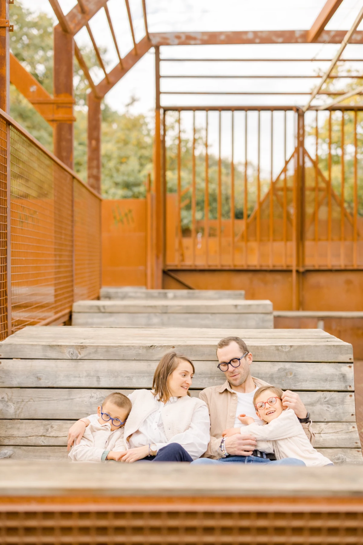 Famille de quatre personnes assise sur des marches en bois dans une structure orangée aux tons chaleureux