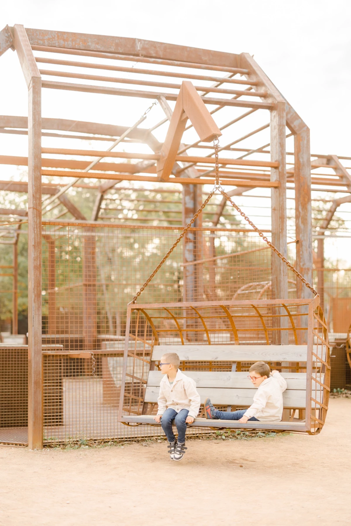 Deux enfants complices assis sur une balançoire en bois dans un parc ensoleillé