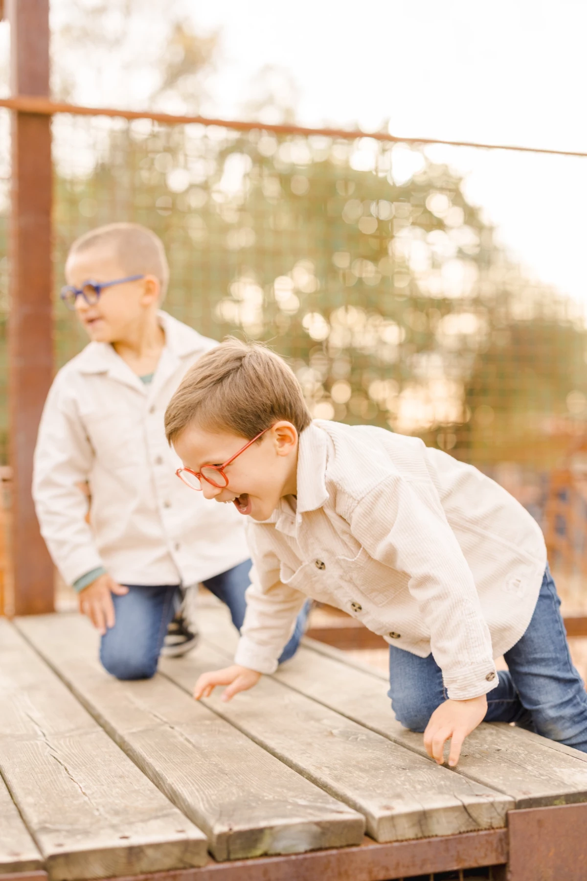 Deux jeunes garçons en chemise blanche jouant sur une plateforme en bois, baignés de lumière naturelle