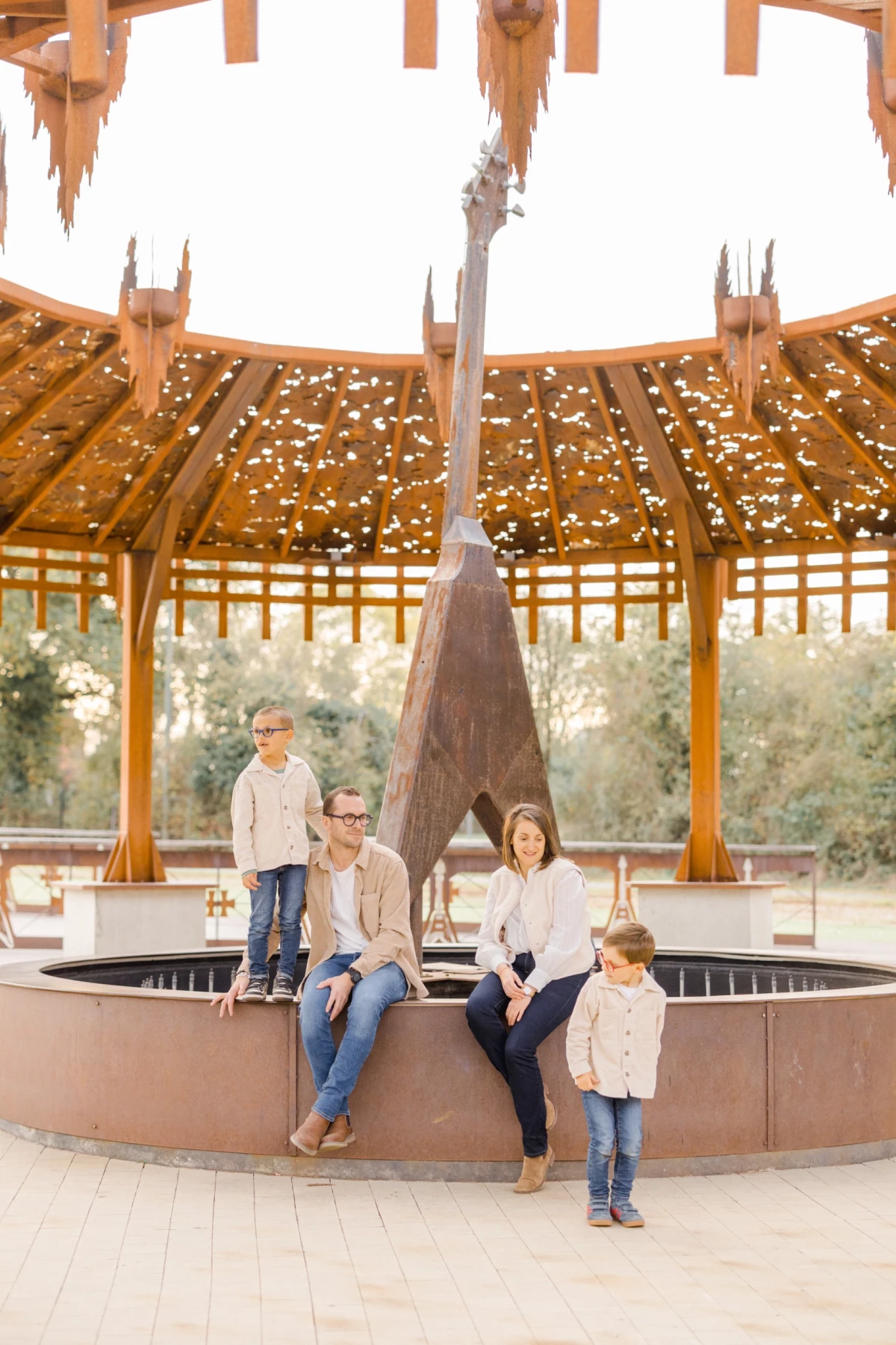 Portrait de famille sous une structure en bois circulaire, parents et deux enfants posant près d'une fontaine