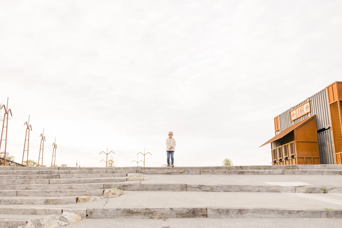 Homme seul contemplant l'horizon depuis un escalier urbain avec éoliennes et bâtiment moderne orangé