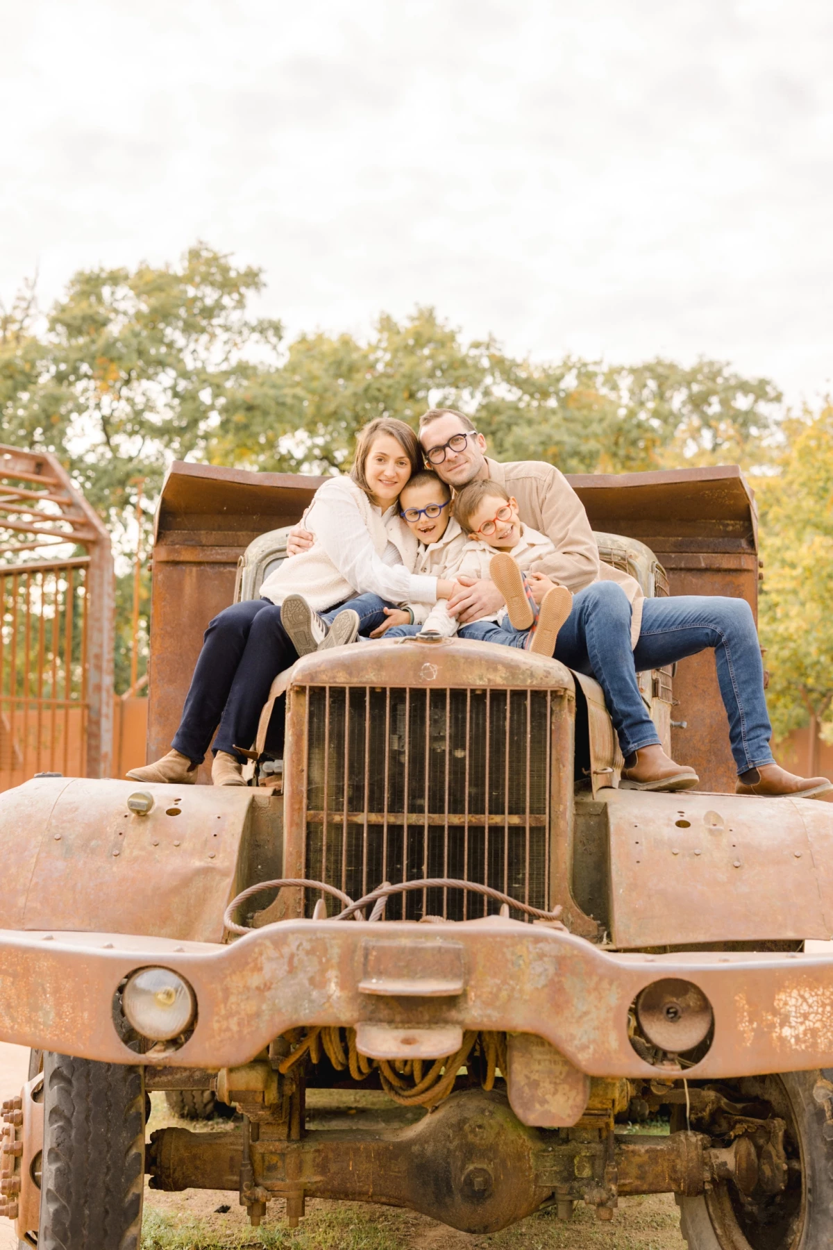 Famille de quatre personnes assise sur un vieux tracteur rouillé, souriant dans un décor automnal