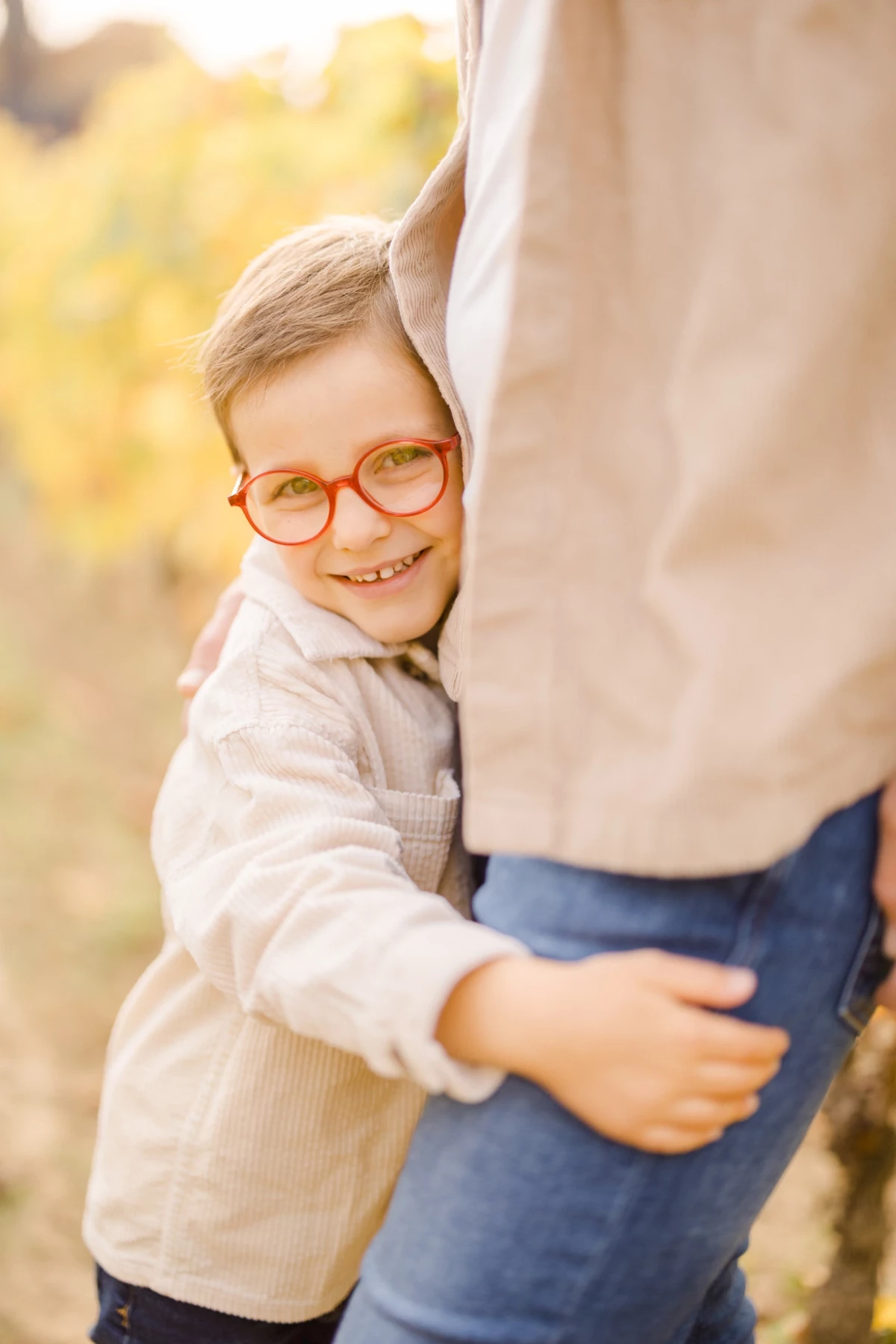 Jeune garçon à lunettes enlace tendrement son parent dans un jardin automnal baigné de lumière dorée