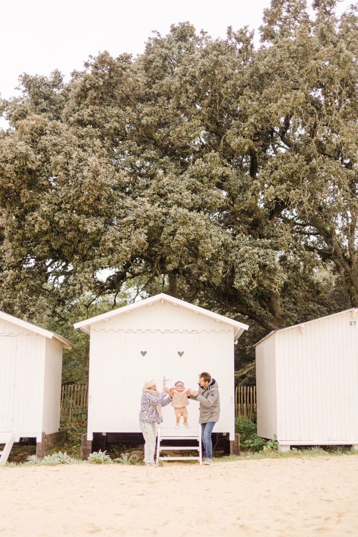 Famille joyeuse avec enfants devant une cabane de plage blanche sous un grand arbre