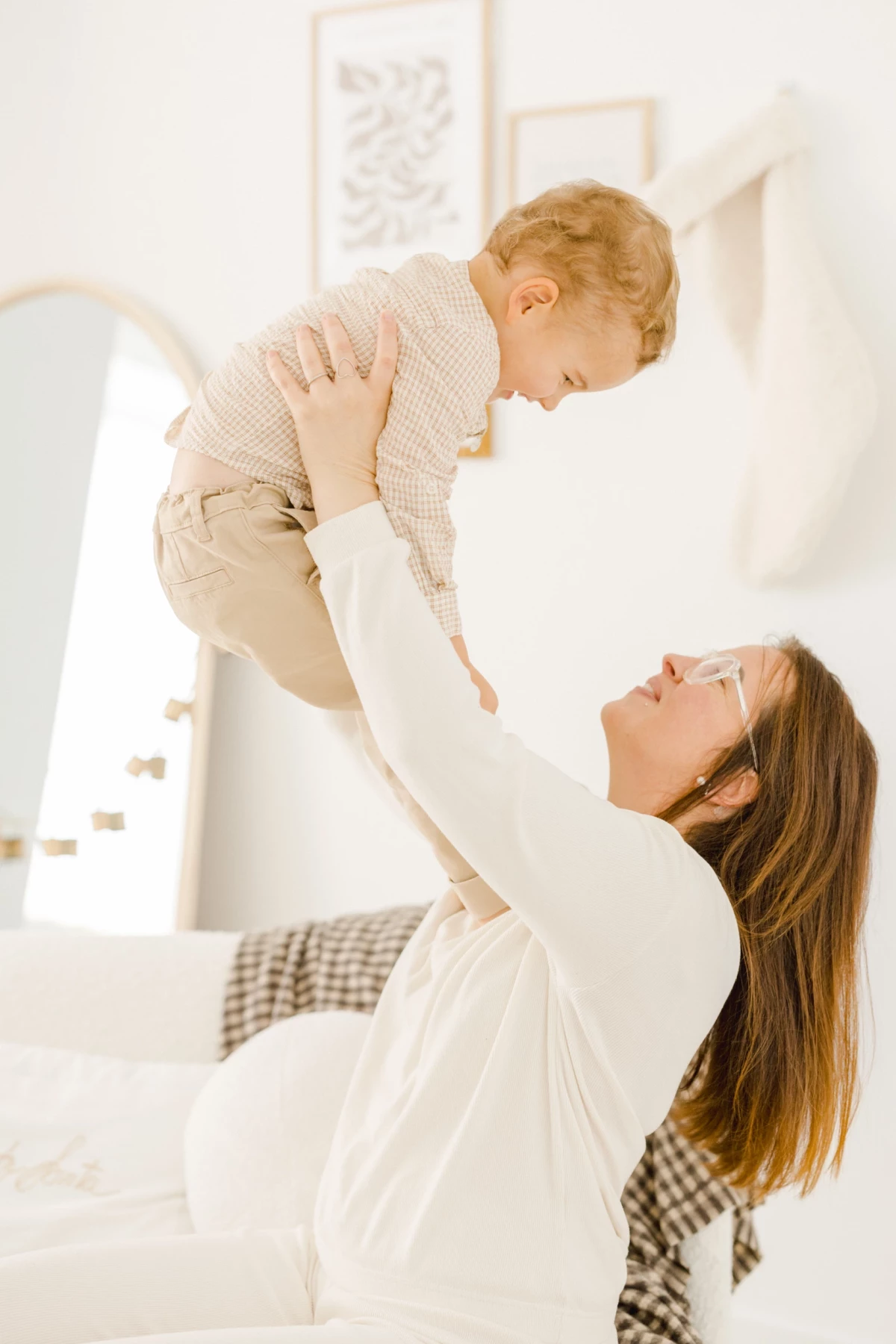 Mère soulevant son jeune enfant en l'air dans un intérieur lumineux aux tons clairs