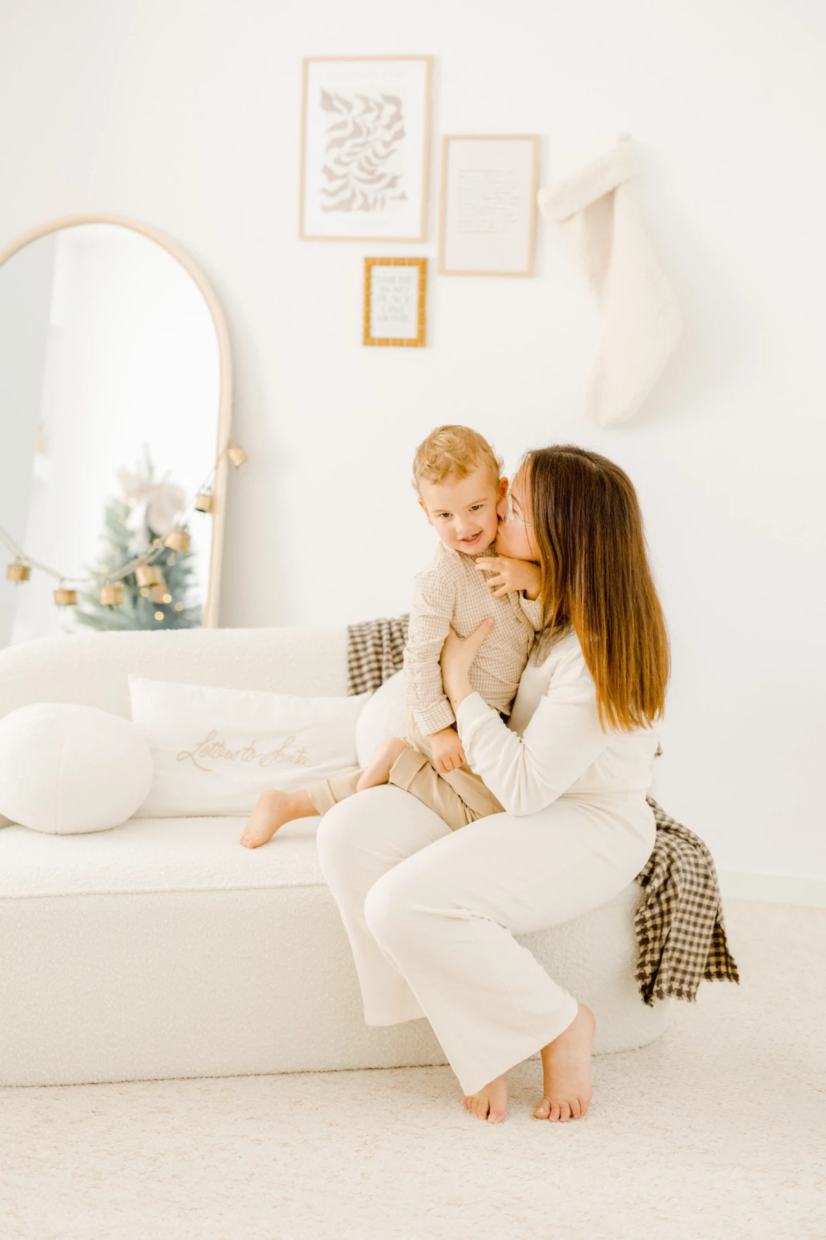 Mère assise sur un lit blanc tenant tendrement son jeune enfant blond dans ses bras
