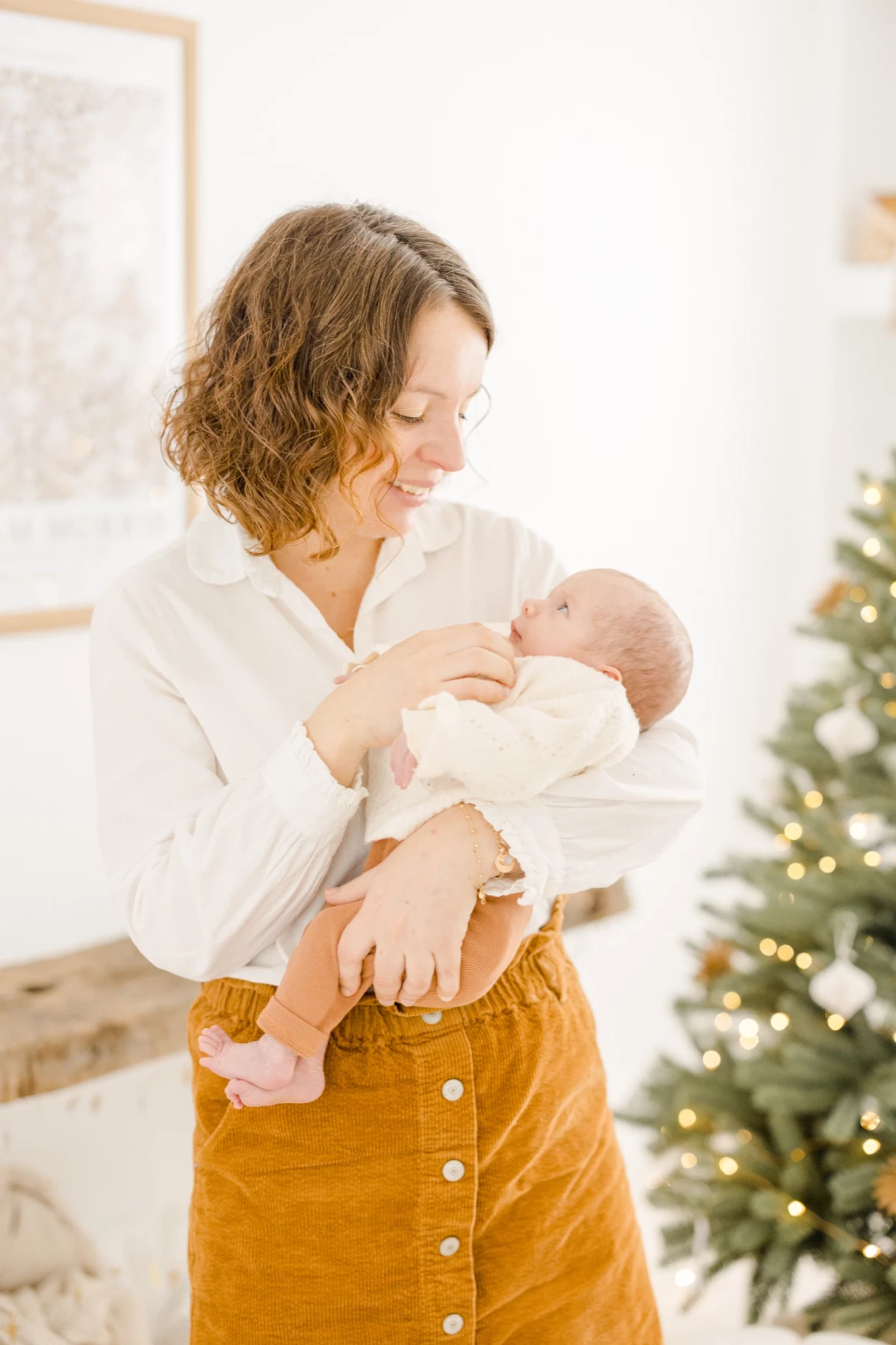 Mère allaitant son nouveau-né près d'un sapin de Noël illuminé, instant de tendresse