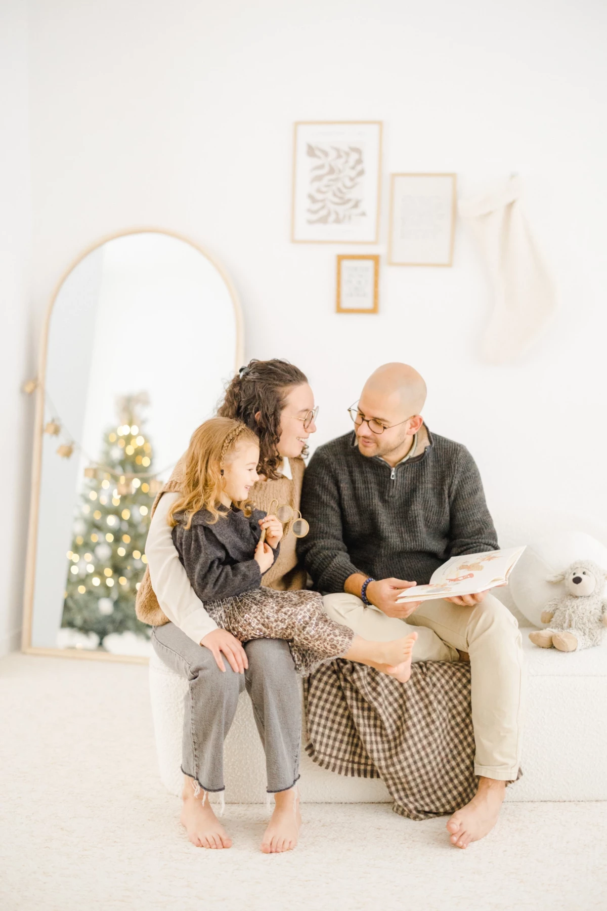 Famille avec enfant partageant un moment de lecture au coin du sapin de Noël dans un studio lumineux