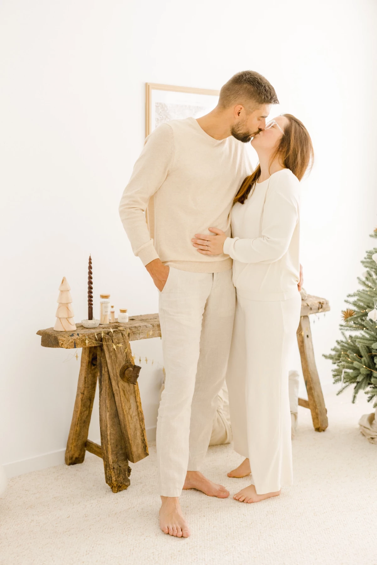 Couple en tenue blanche s'embrassant tendrement lors d'une séance photo grossesse dans un décor de Noël