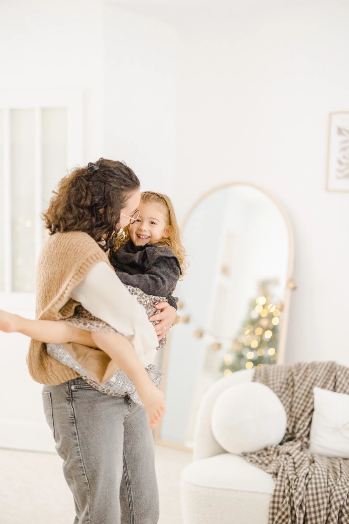 Mère enlaçant tendrement sa petite fille dans un intérieur blanc décoré pour Noël