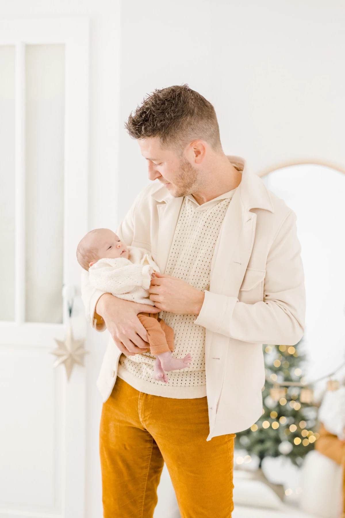 Jeune père en tenue beige et pantalon jaune tenant tendrement son nouveau-né dans les bras