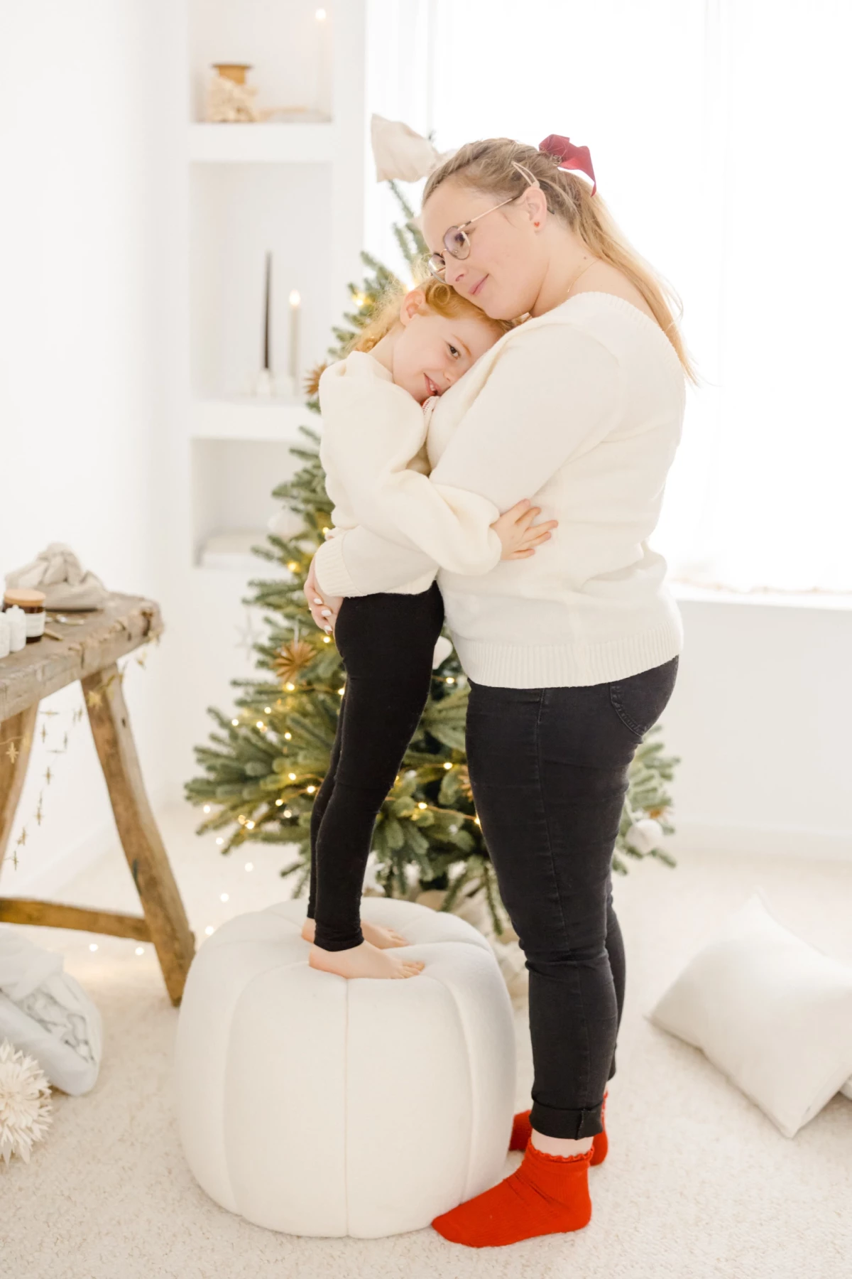 Mère et enfant enlacés dans un tendre câlin de Noël, vêtus de blanc devant un sapin illuminé