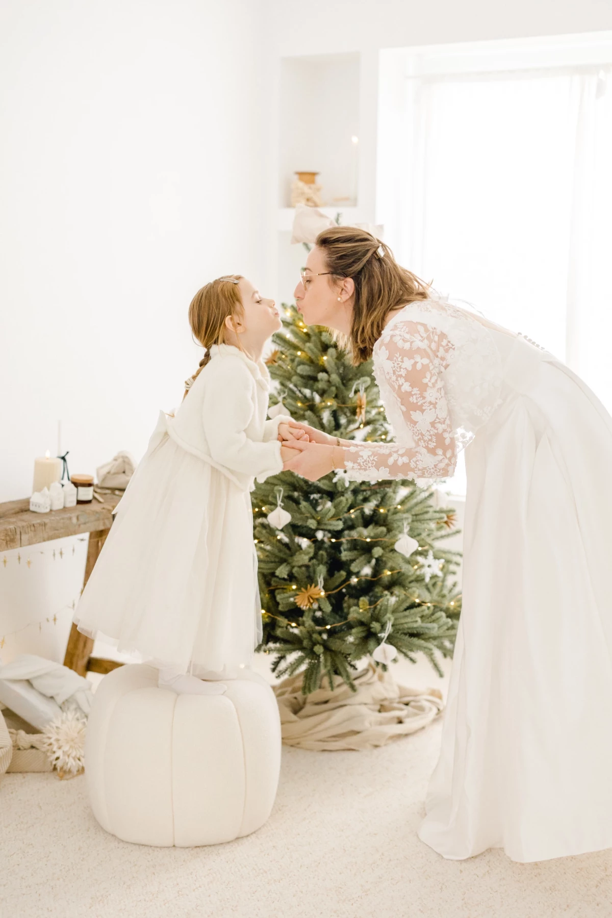 Mariée en robe blanche partageant un tendre baiser avec sa fille devant le sapin de Noël décoré