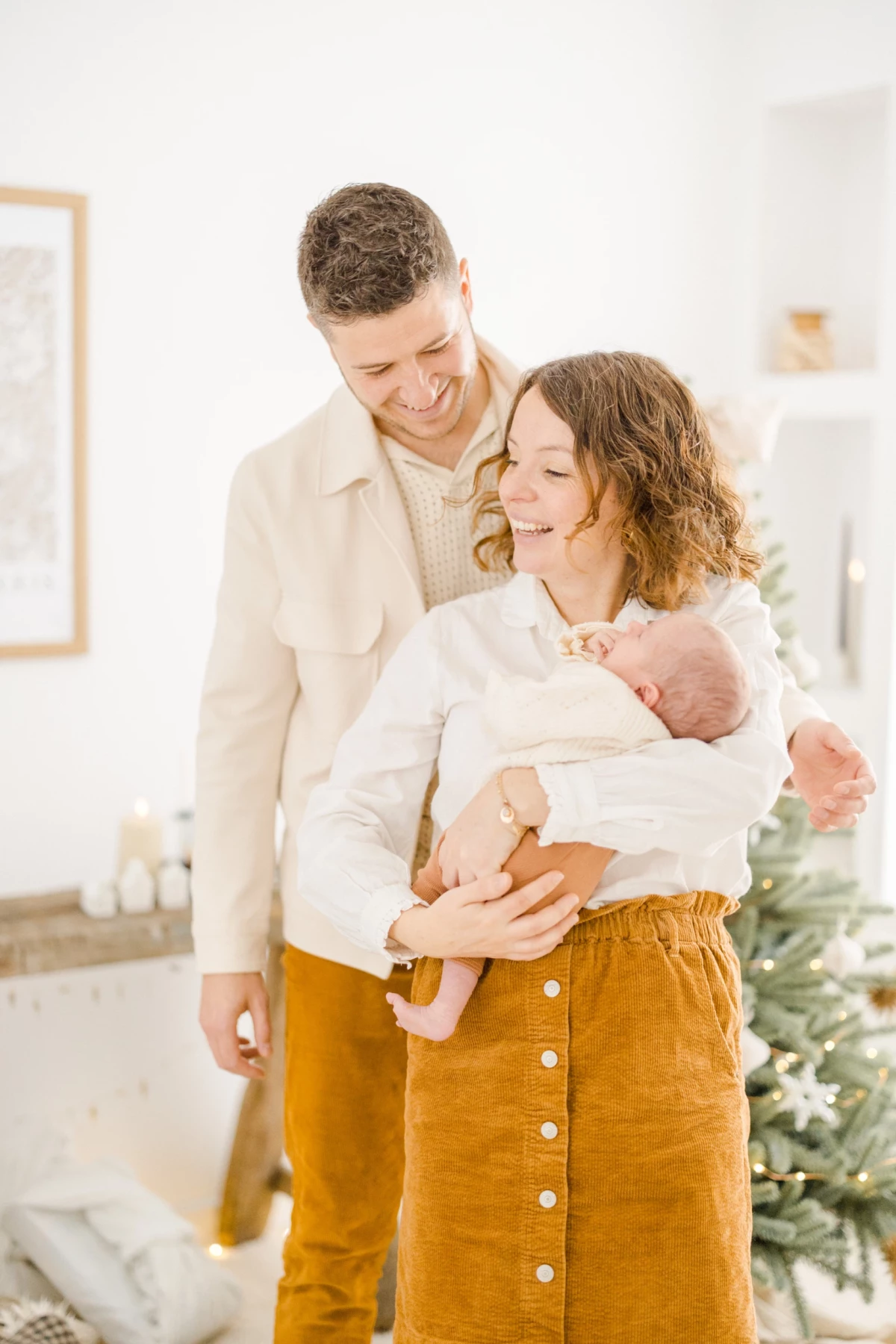 Jeunes parents enlacés avec leur nouveau-né dans un intérieur lumineux aux tons beiges et ocre