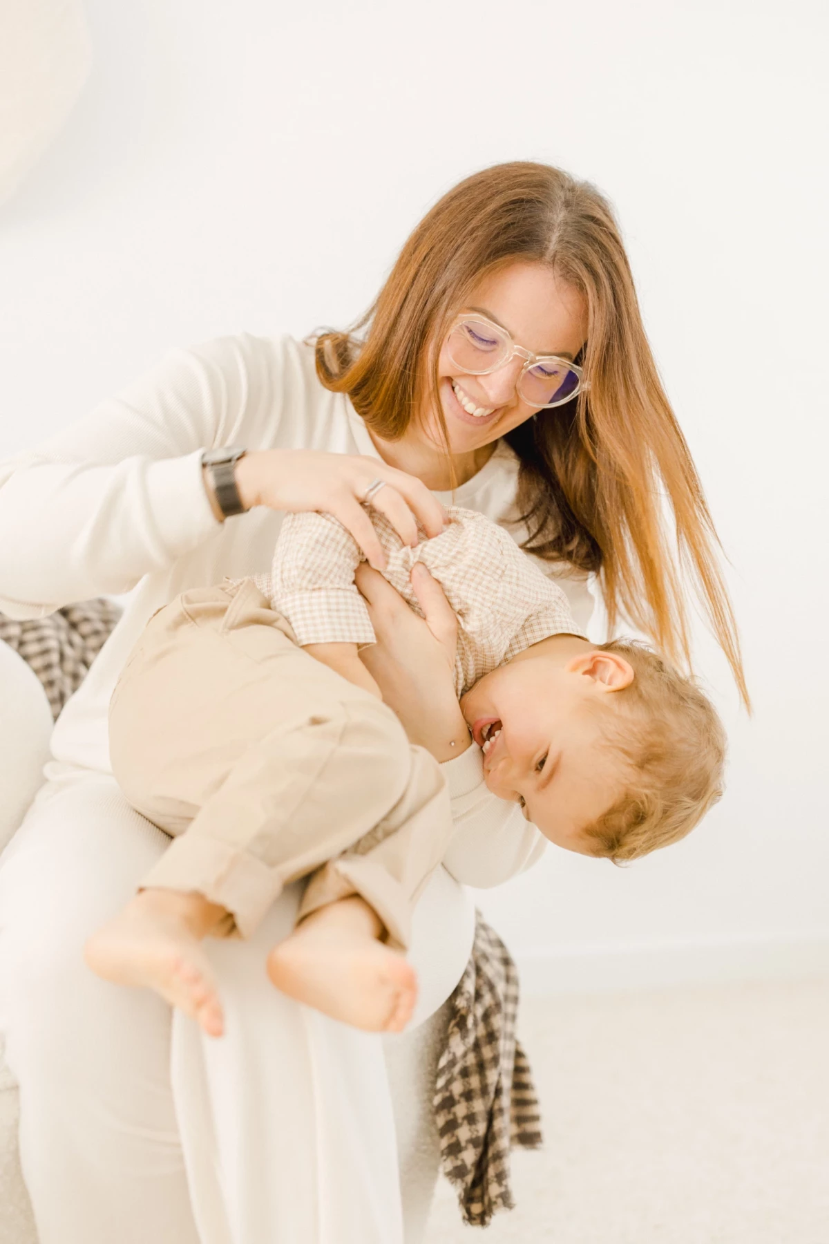 Mère souriante allaitant son bébé dans une robe blanche fluide sur fond clair et lumineux