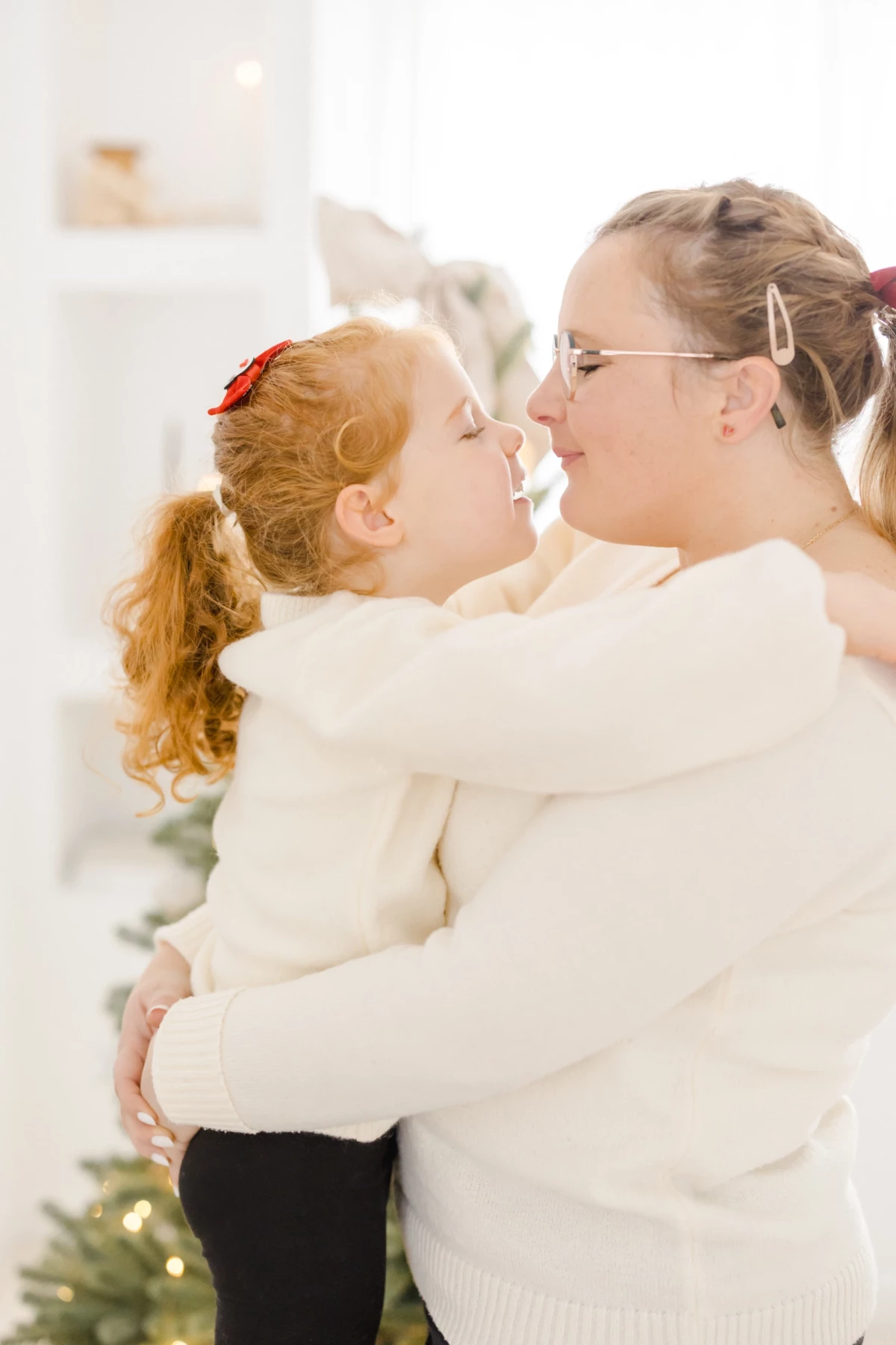 Mère et fille en pulls blancs se faisant un bisou eskimo lors d'une séance photo de Noël en famille