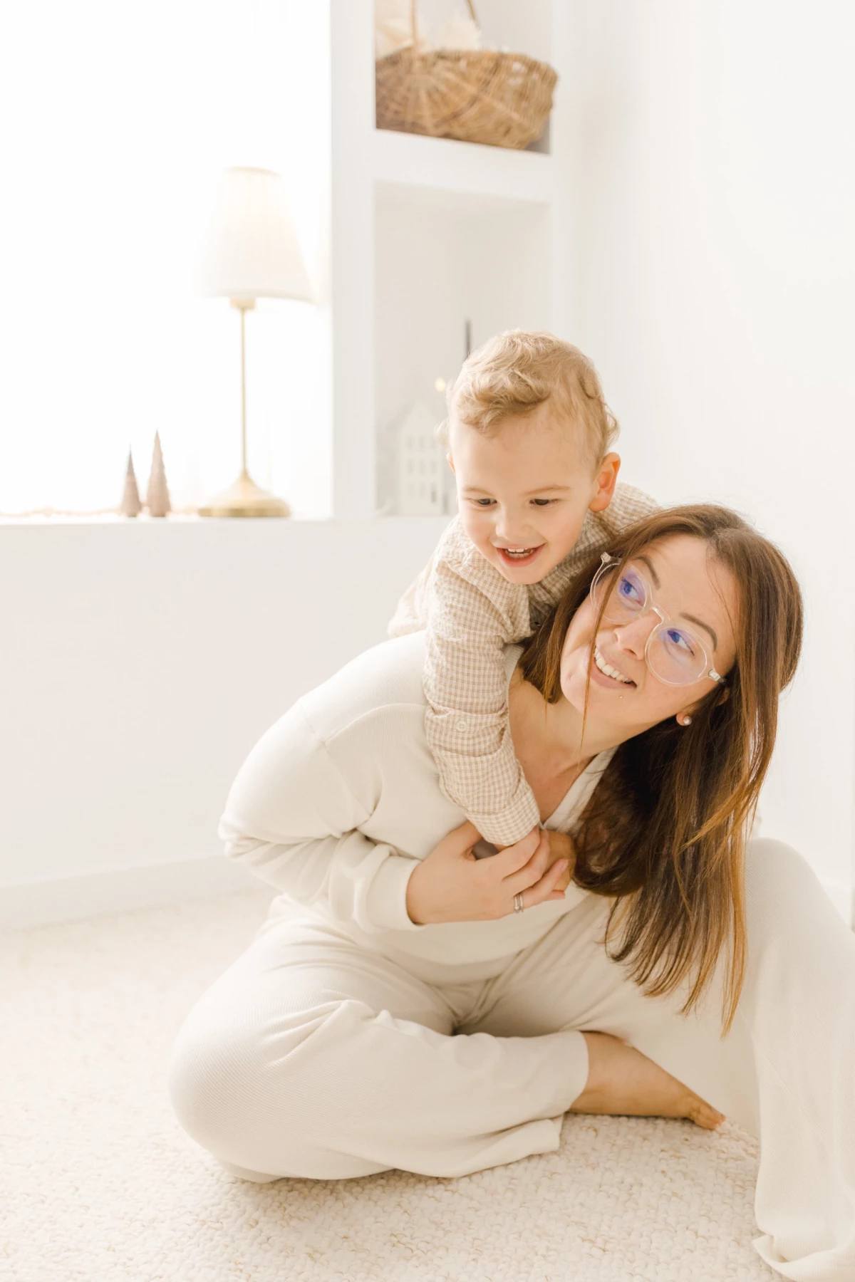 Mère souriante portant son enfant dans ses bras lors d'une séance photo famille en studio lumineux