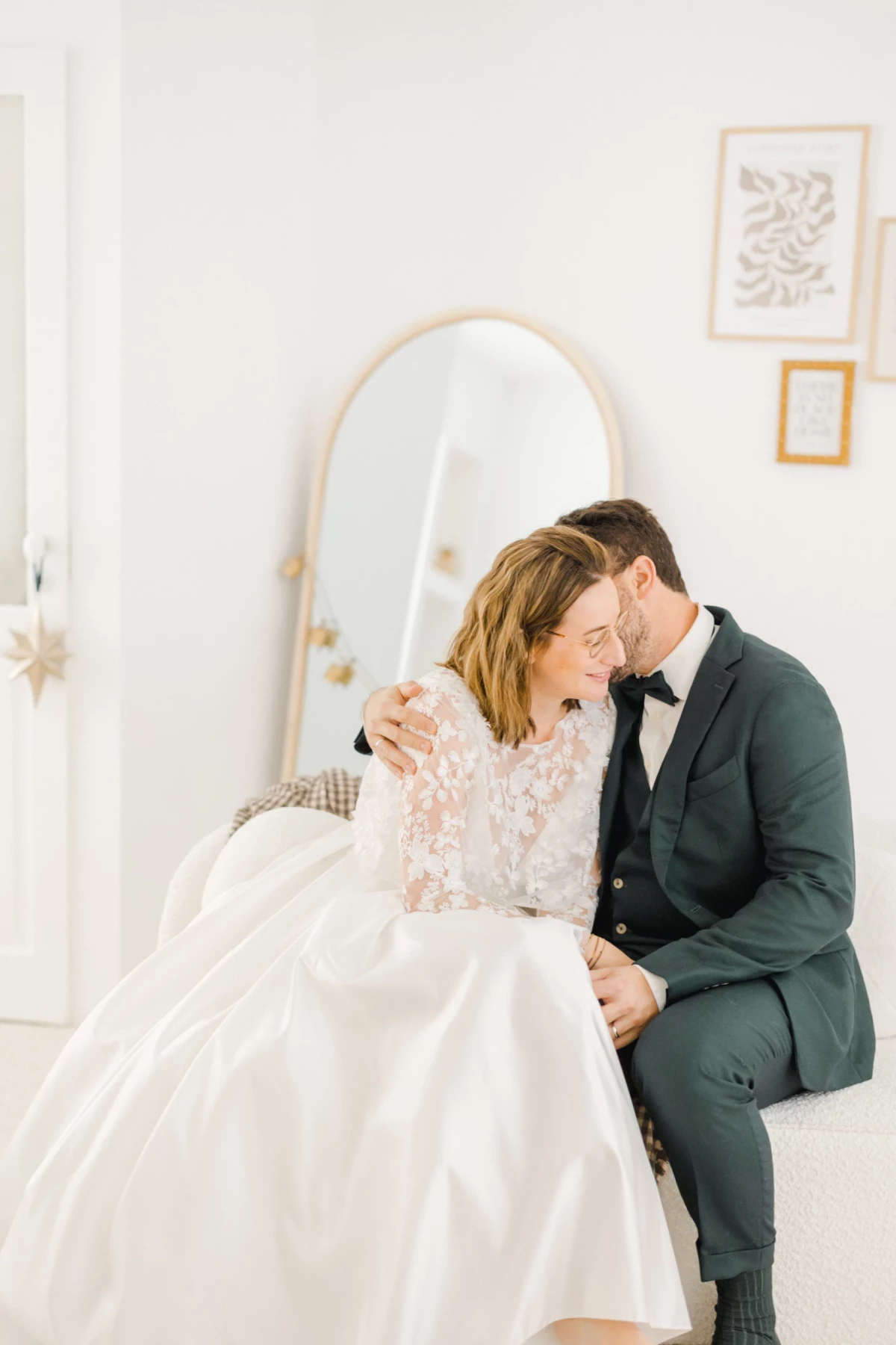 Couple de mariés assis enlacés dans un studio épuré aux tons beige et blanc