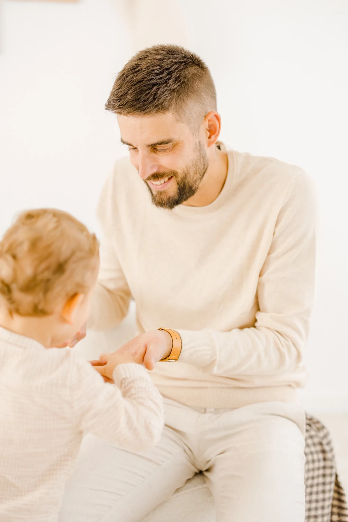 Père et fils en tenue beige échangeant un jouet en bois dans une atmosphère douce et complice