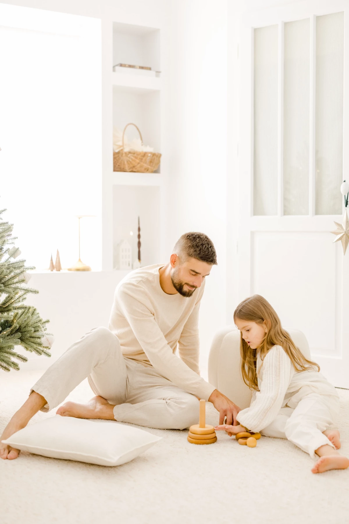 Père et fille jouant ensemble avec des jouets en bois dans un intérieur épuré aux tons beiges