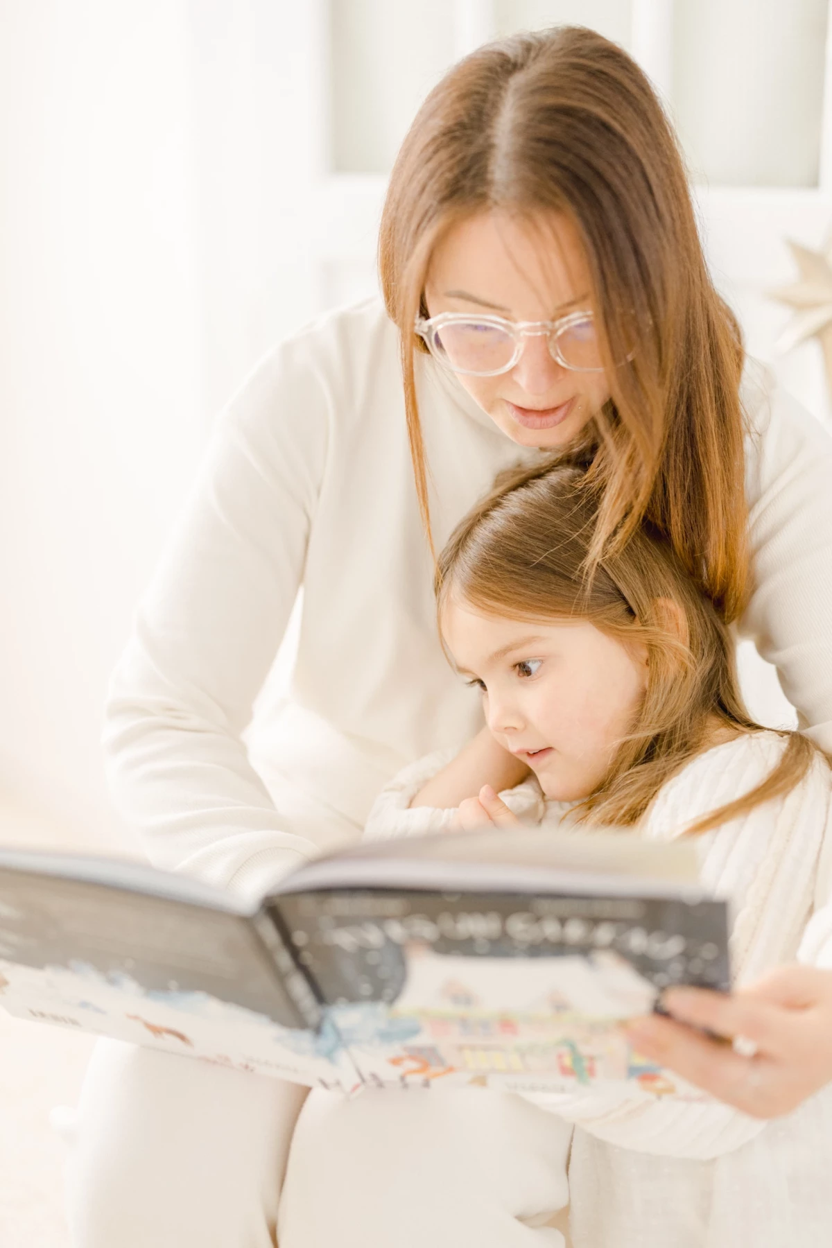 Mère et fille lisant ensemble un livre, enlacées dans une douce complicité sur un canapé blanc