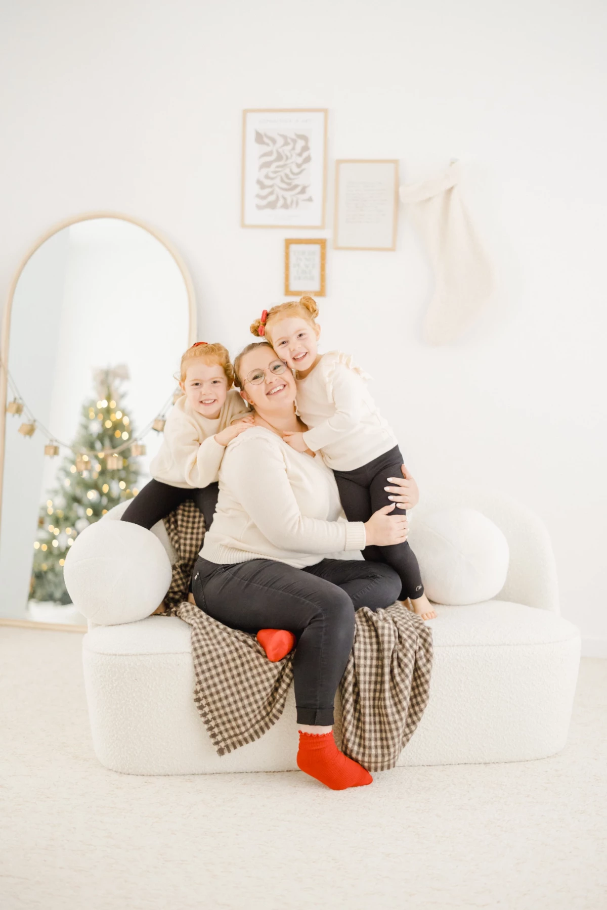 Mère et ses deux filles enlacées sur un fauteuil blanc dans un décor de Noël lumineux