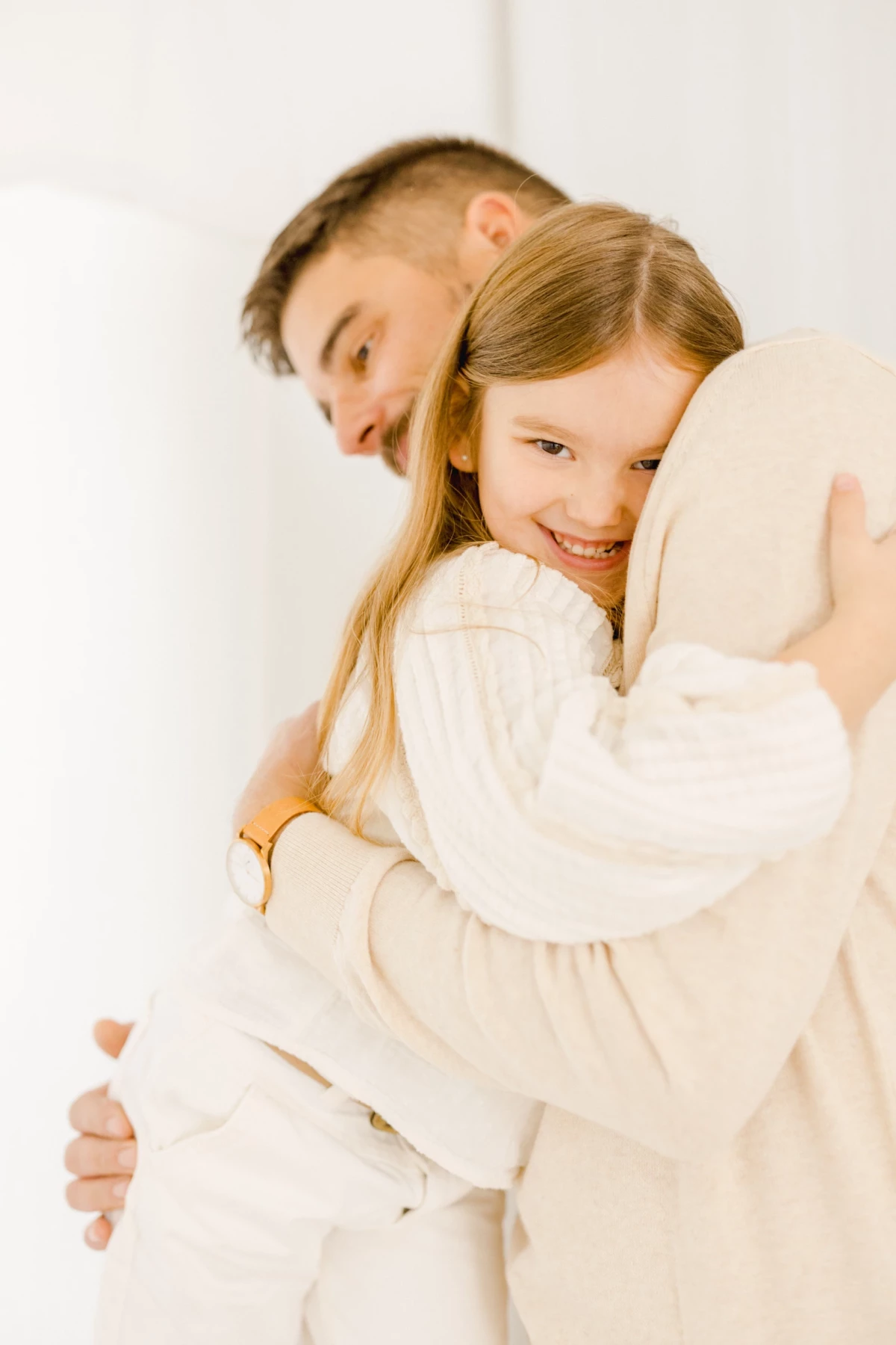 Père et fille enlacés dans un câlin tendre, vêtus de blanc, sur fond lumineux et épuré