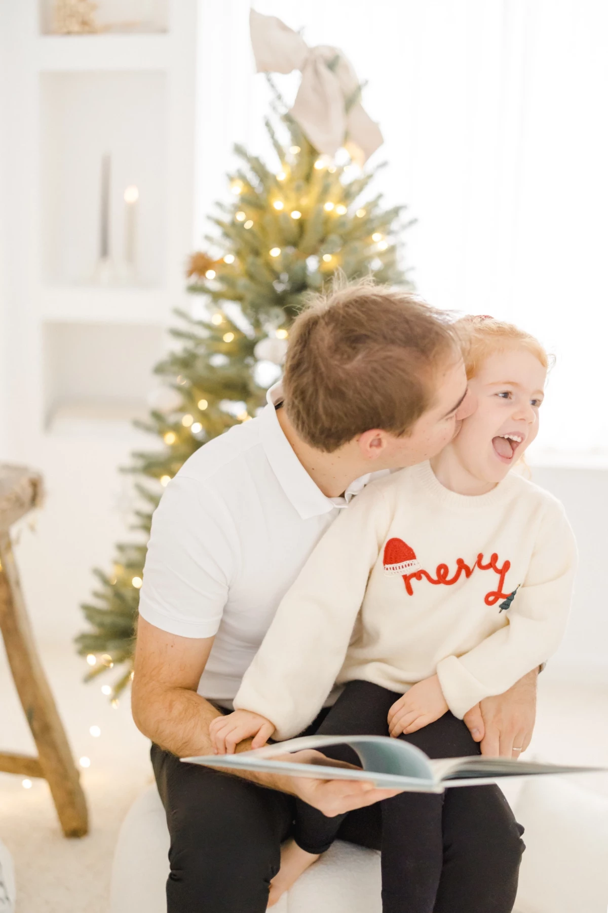 Père et fils lisant ensemble devant un sapin de Noël illuminé, moment de complicité familiale