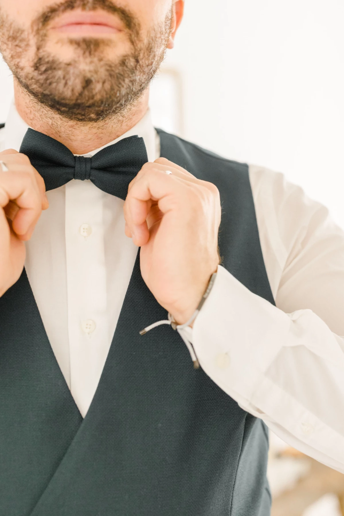 Marié ajustant son nœud papillon noir sur chemise blanche et gilet gris anthracite lors des préparatifs