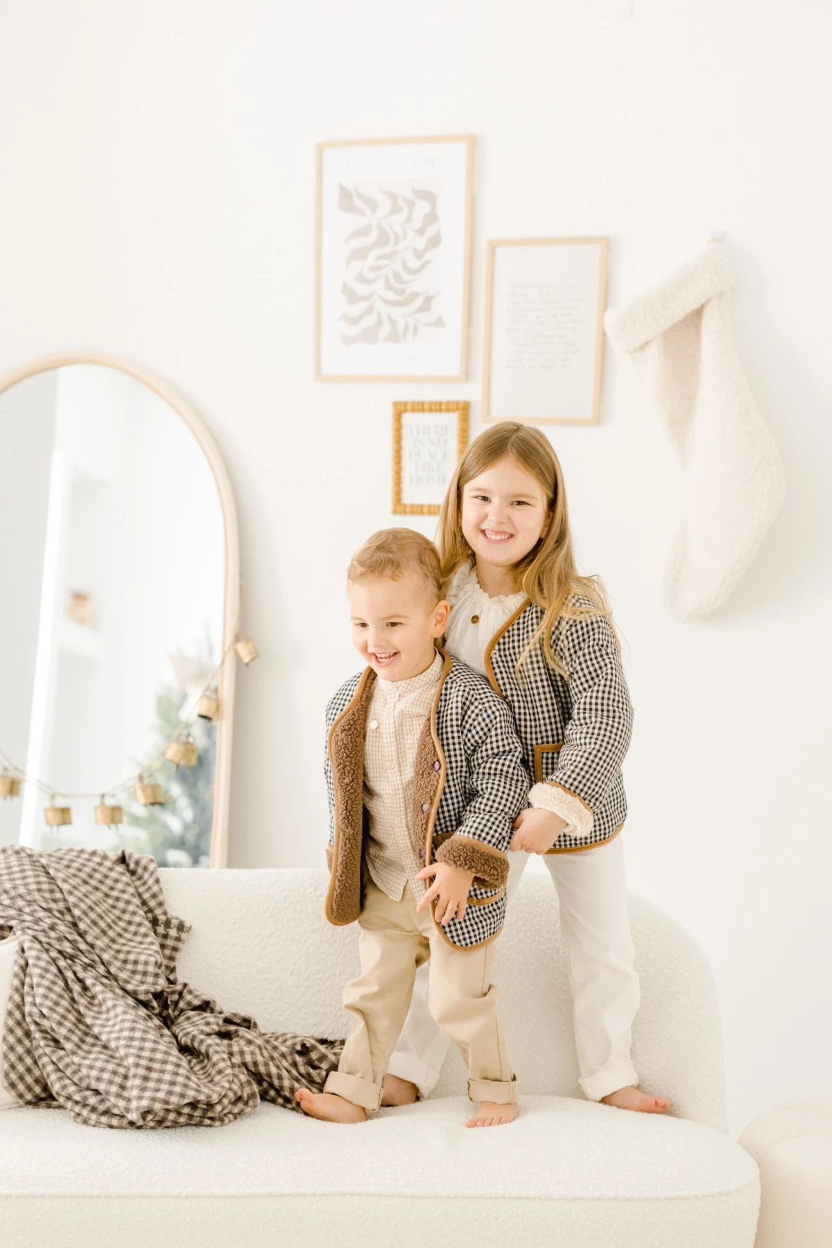 Deux enfants complices en tenue beige et marron posant ensemble sur un lit blanc dans un décor épuré