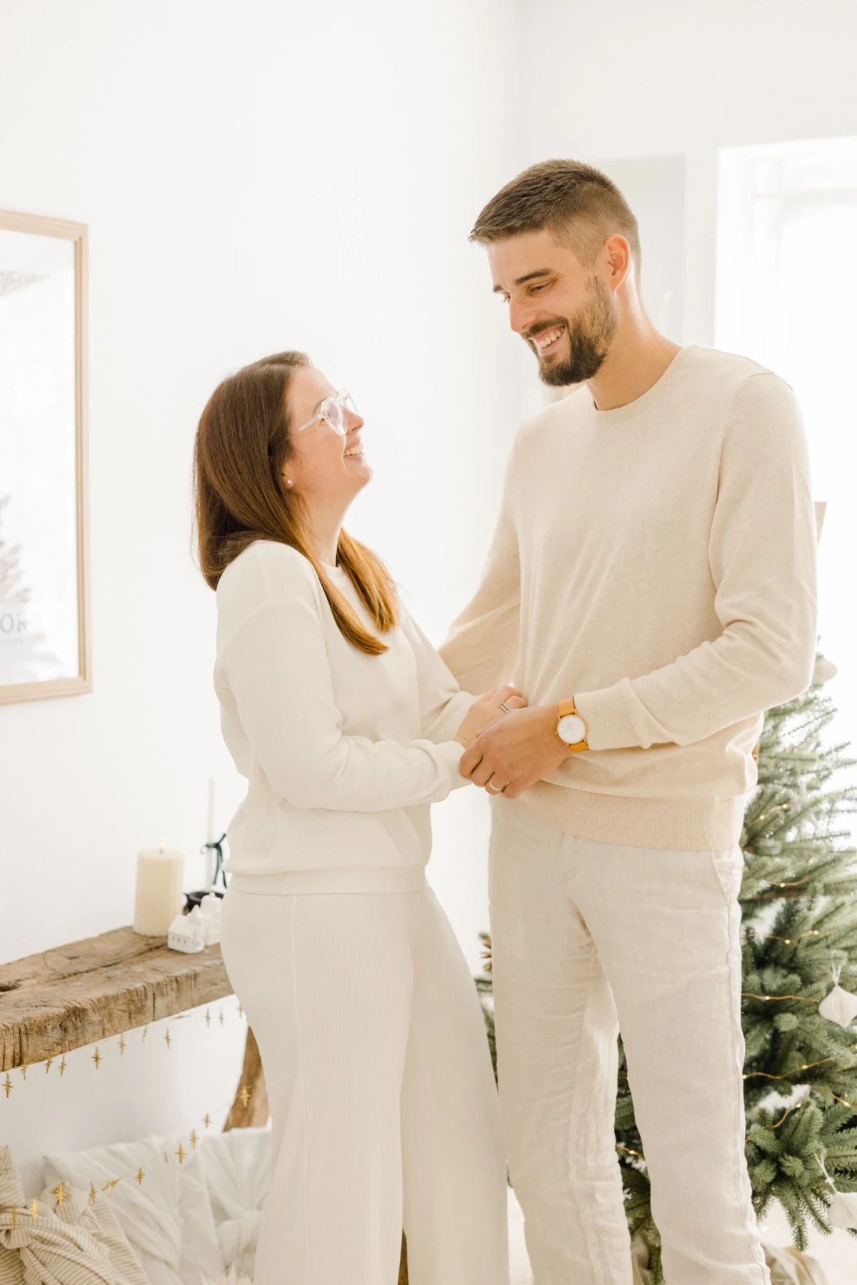 Couple complice en tenues beiges se tenant les mains dans un intérieur blanc décoré pour Noël