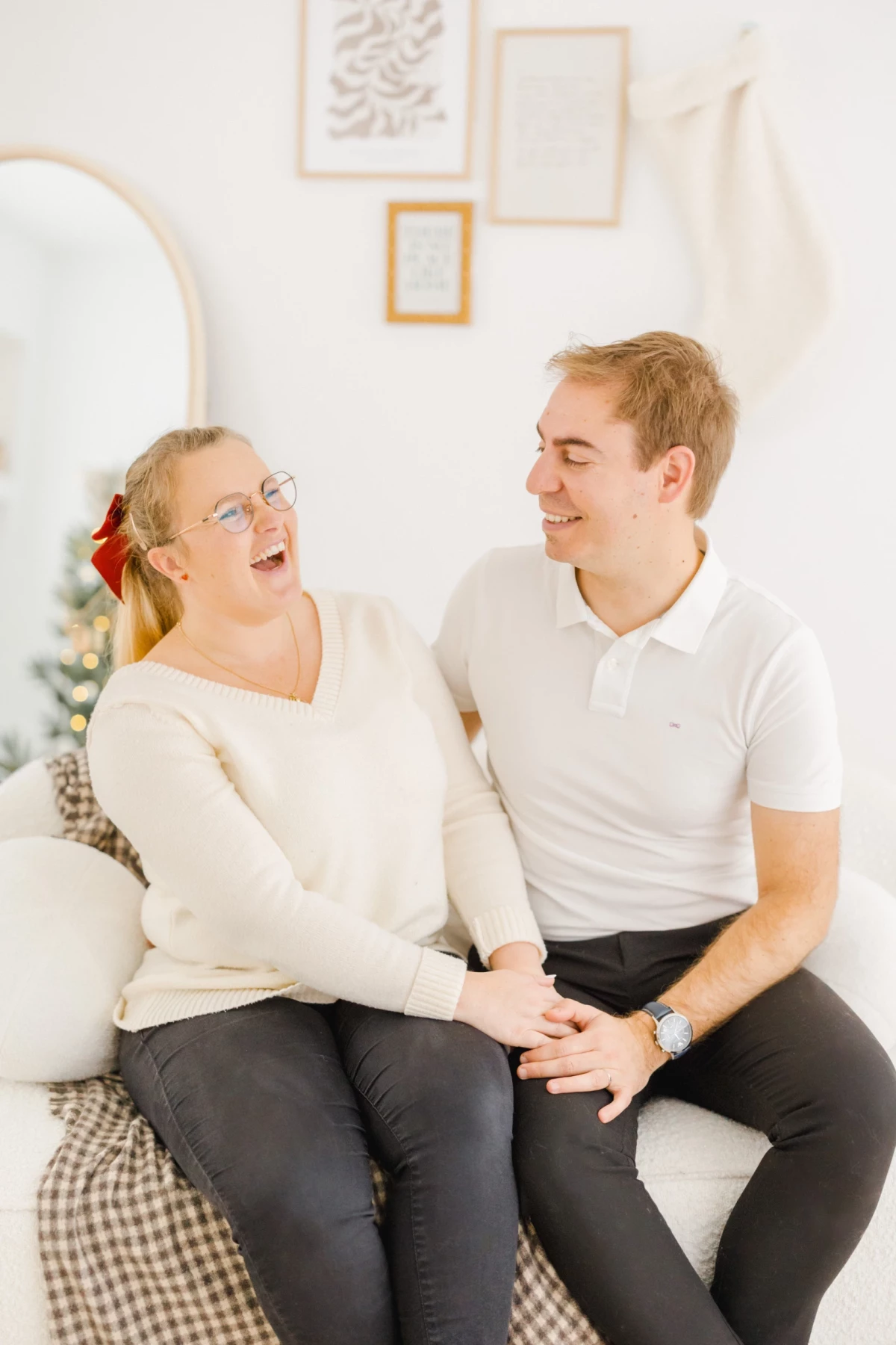 Couple complice souriant assis sur un canapé beige dans un décor blanc lumineux et épuré