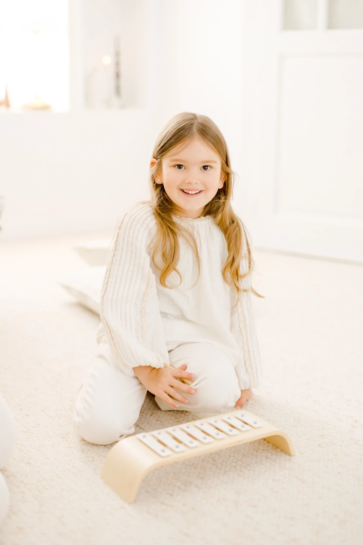 Petite fille souriante en tenue blanche assise en studio lumineux avec un instrument de musique en bois