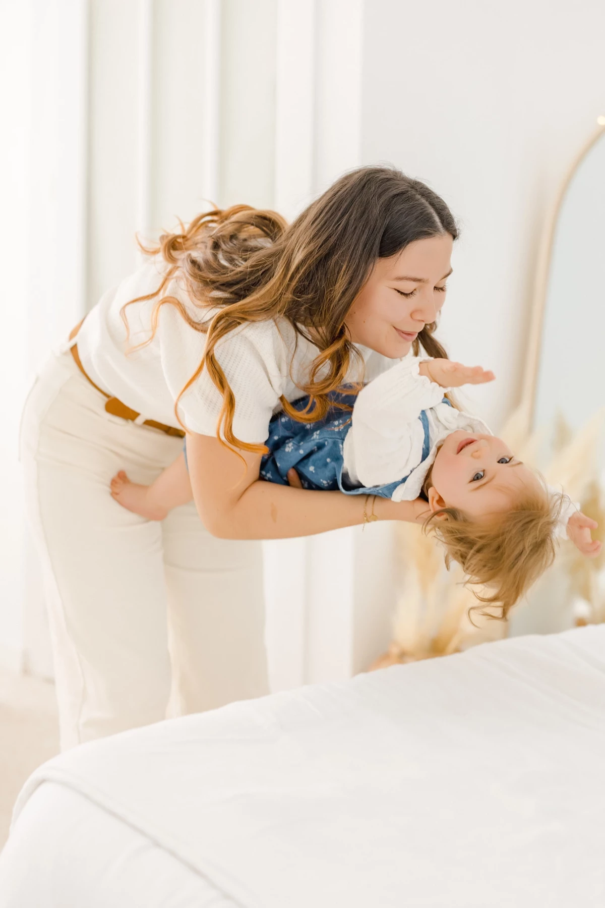 Séance famille au studio : une maman soulève sa petite fille en robe blanche, partageant un moment de complicité et de joie pure