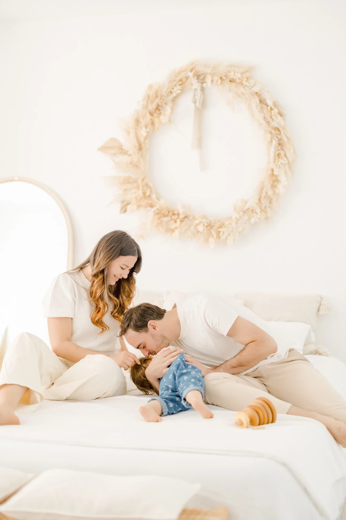 Séance famille au studio : parents et leur petite fille partagent un moment de complicité et de tendresse sur un lit blanc immaculé