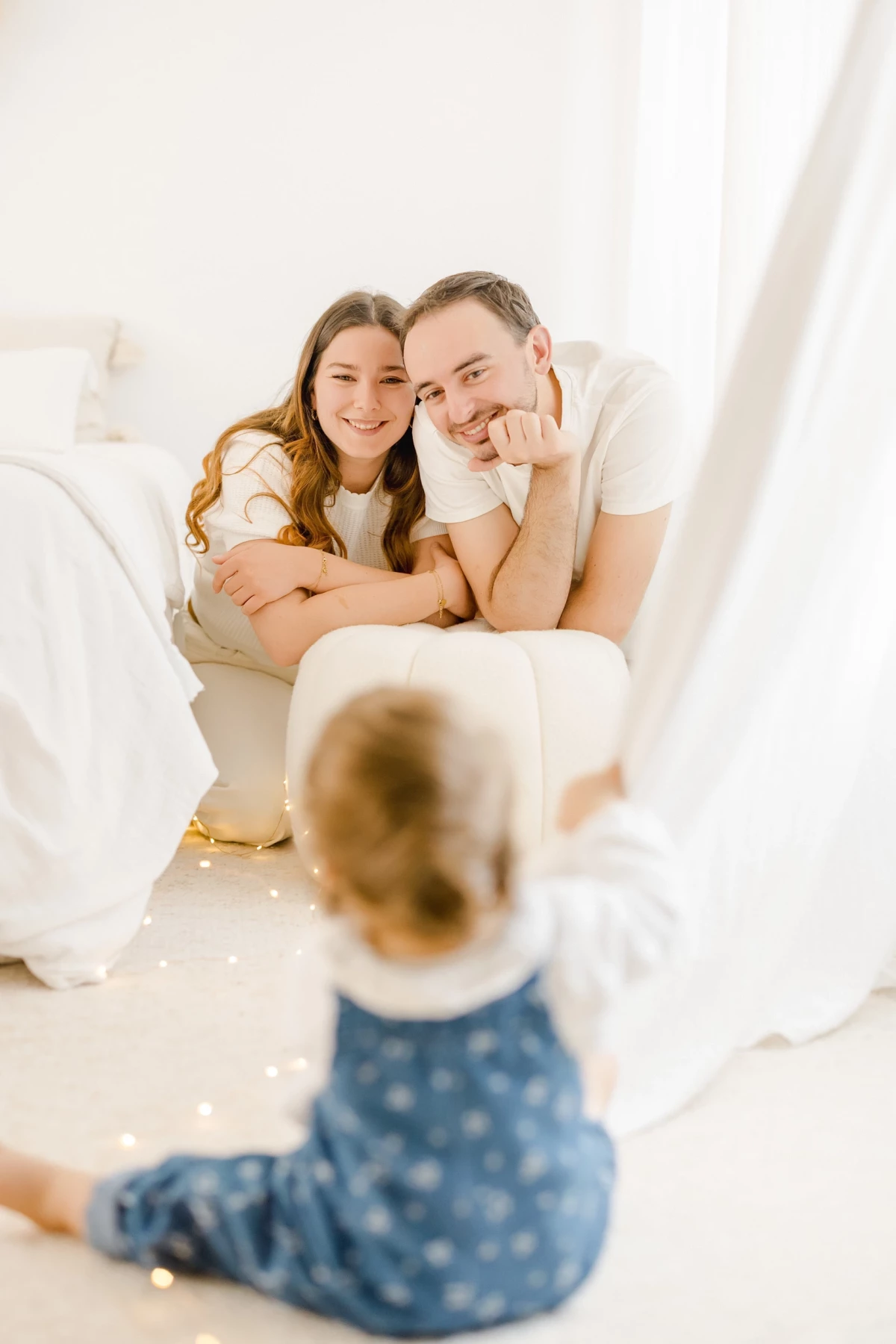 Séance famille au studio : parents enlacés observent leur petite fille avec tendresse dans une ambiance lumineuse et naturelle
