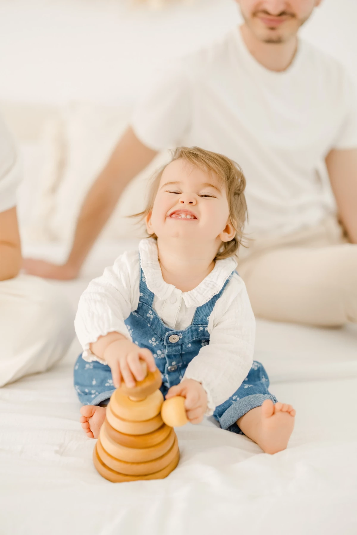 Séance famille au studio : petite fille joyeuse jouant avec une pyramide en bois, instant de bonheur naturel et lumineux