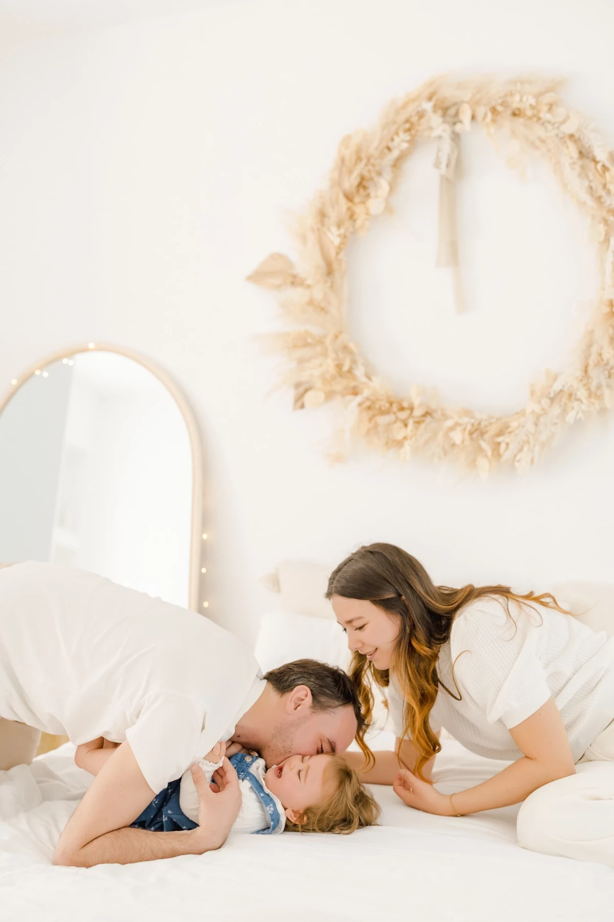 Séance famille au studio : parents embrassent leur petite fille dans une ambiance douce et lumineuse sur fond blanc