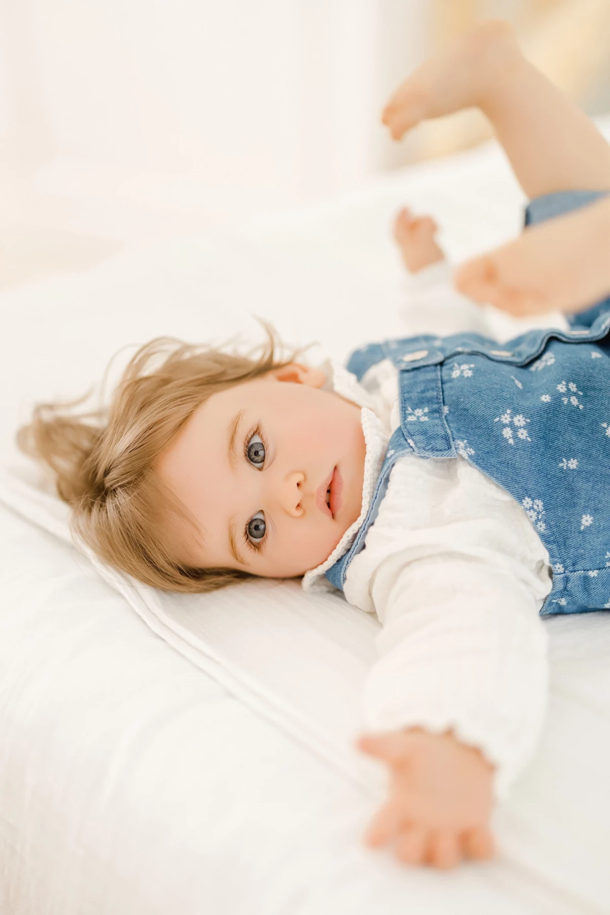 Séance famille au studio : petite fille aux yeux clairs allongée, regard doux et naturel dans une ambiance lumineuse et épurée