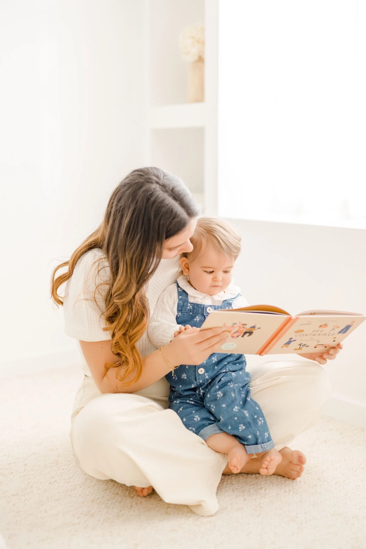 Séance famille au studio : mère et fille partagent un moment de lecture complice dans une ambiance douce et lumineuse