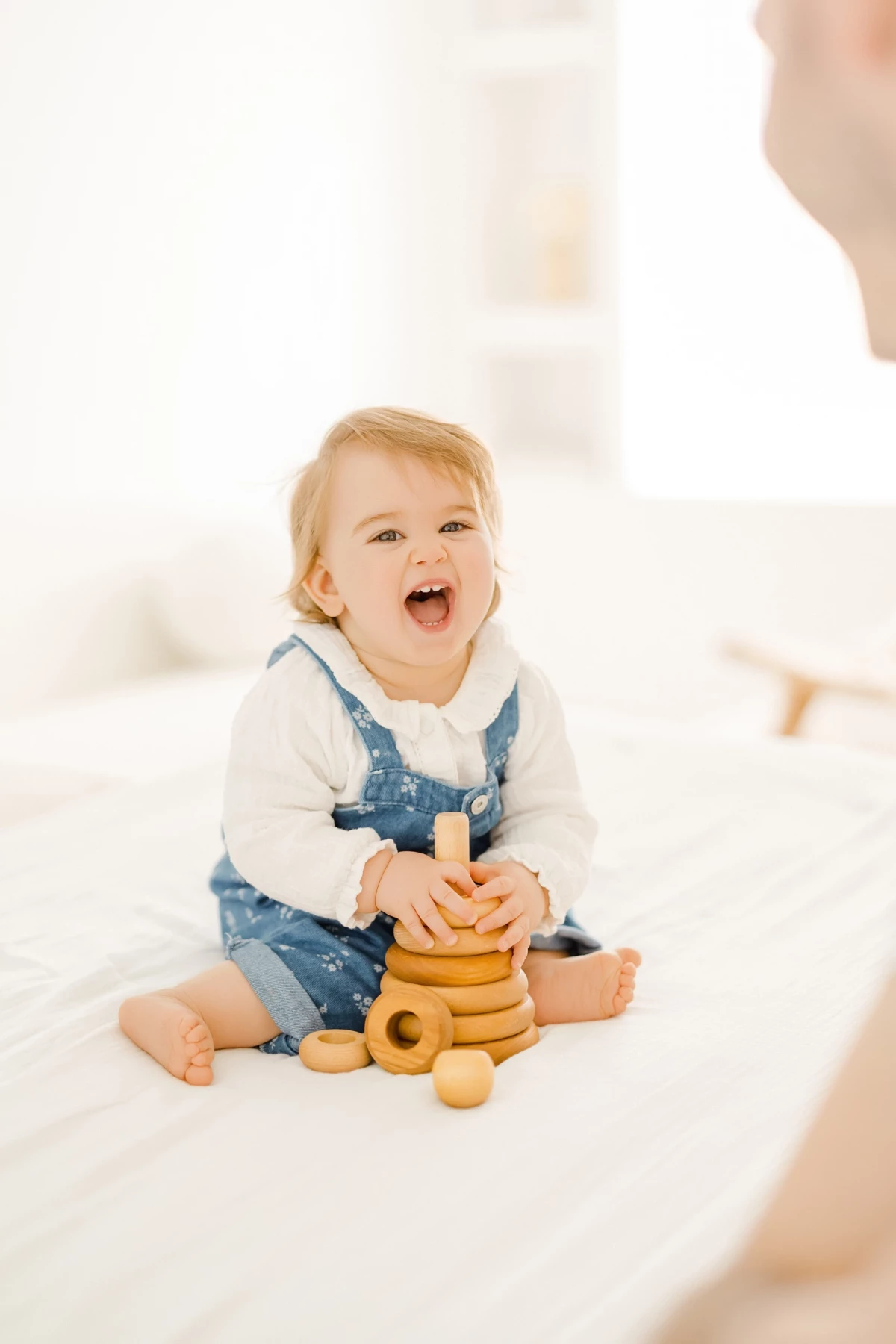 Séance famille au studio : bébé tout sourire joue avec un jouet en bois dans une ambiance lumineuse et naturelle