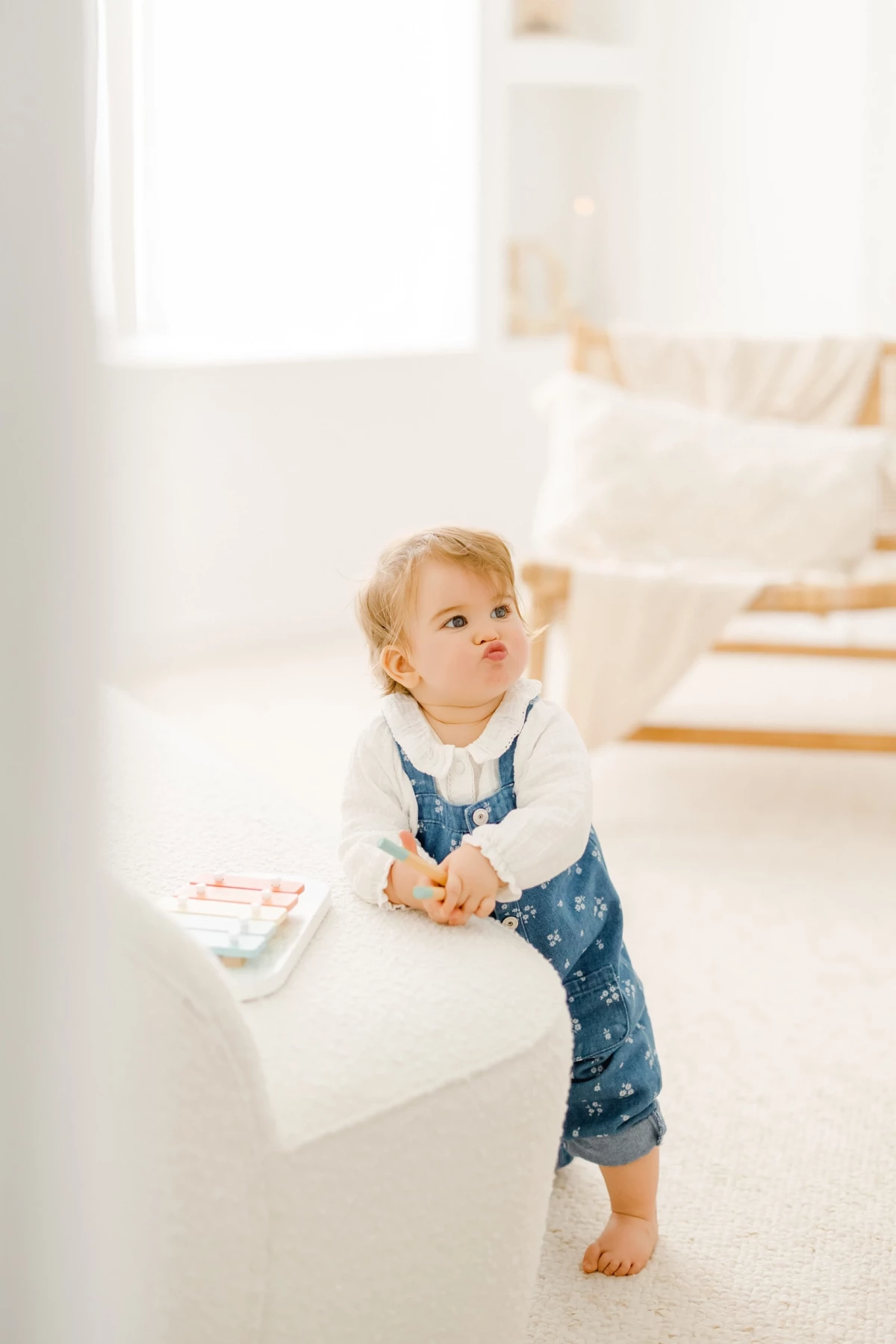 Séance famille au studio : petite fille blonde en salopette regarde en l'air avec émerveillement dans une ambiance lumineuse et naturelle