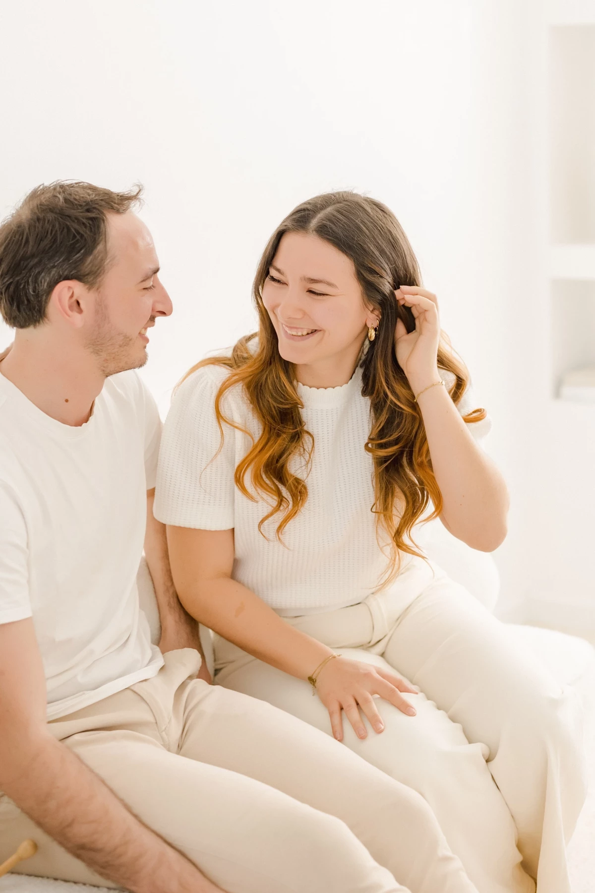 Séance famille au studio : couple complice échange un regard tendre dans une ambiance lumineuse et naturelle, tons beige et blanc