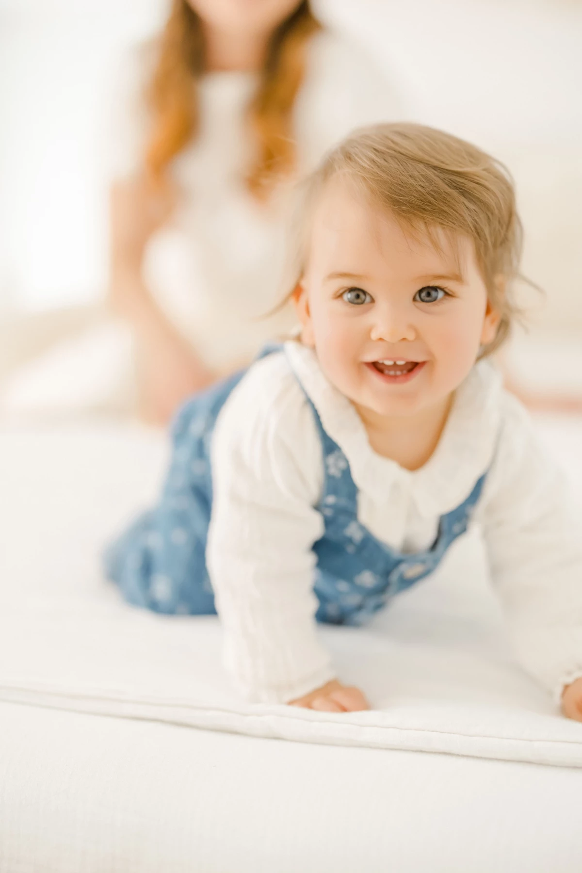 Séance famille au studio : petite fille souriante en robe blanche et pantalon bleu capturée dans un moment de joie naturelle