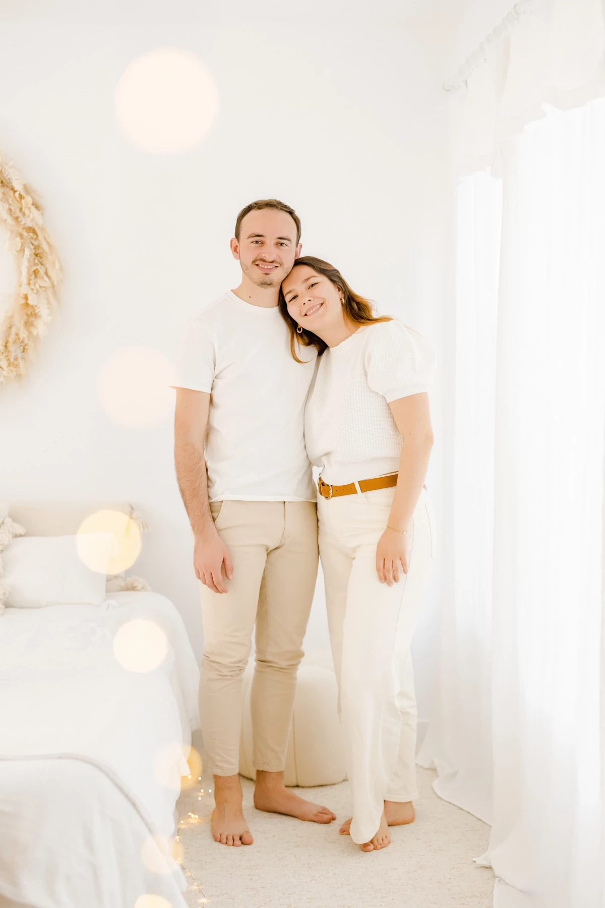 Séance famille en studio : parents complices et souriants dans une ambiance lumineuse et épurée, tons beige et blanc naturels