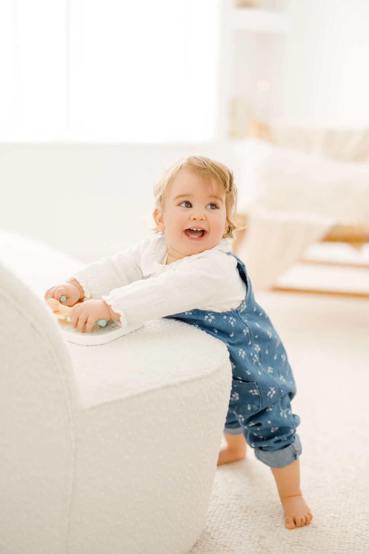 Séance famille en studio : petite fille blonde souriante joue avec un jouet, instant de joie spontanée et naturelle