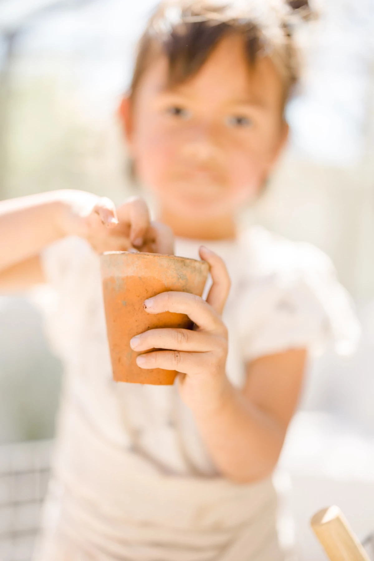 Séance famille Vendée : fillette tient un pot de terre lors d'un atelier jardinage en verrière, lumière naturelle douce