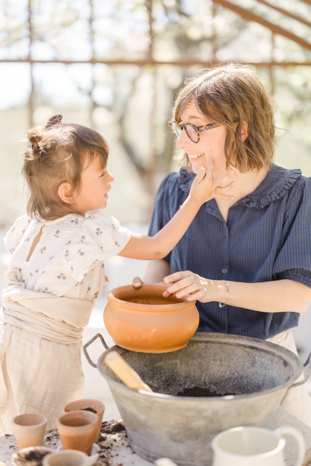 Séance famille dans une verrière : mère et fille complices lors d'un atelier jardinage, lumière naturelle printanière