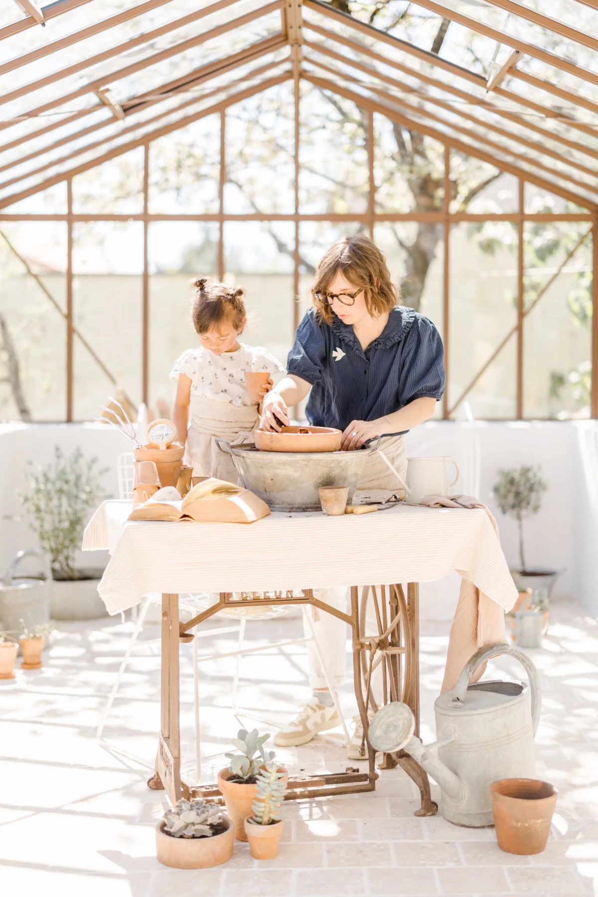 Séance famille au printemps : maman et sa petite fille partagent un moment de jardinage dans une verrière lumineuse