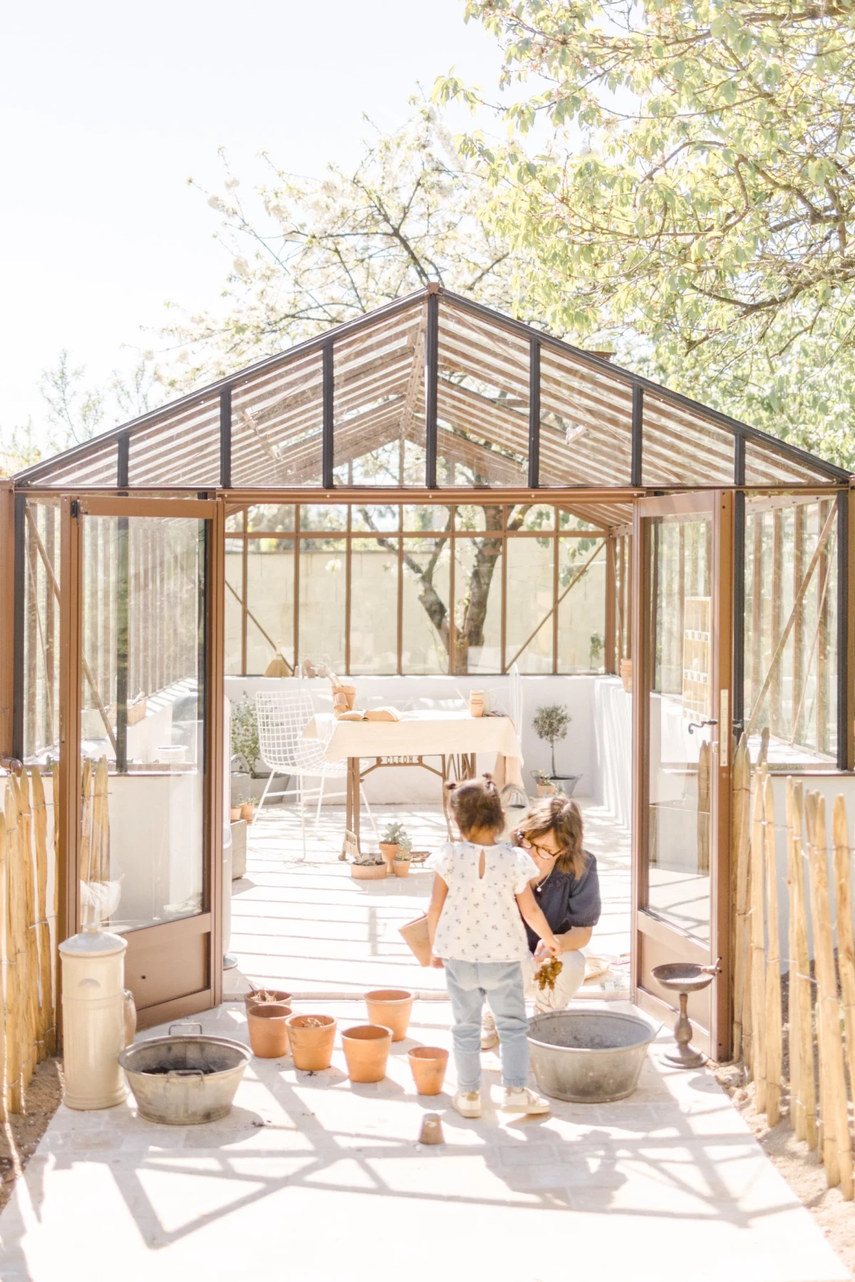Séance famille dans une verrière : mère et fille jardinent ensemble dans une lumière printanière douce et naturelle